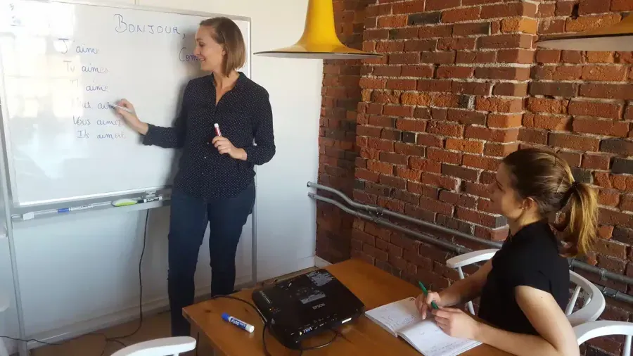 French teacher writing verb conjugations on whiteboard while student studies: TEF and TCF compréhension écrite reading practice in Vancouver