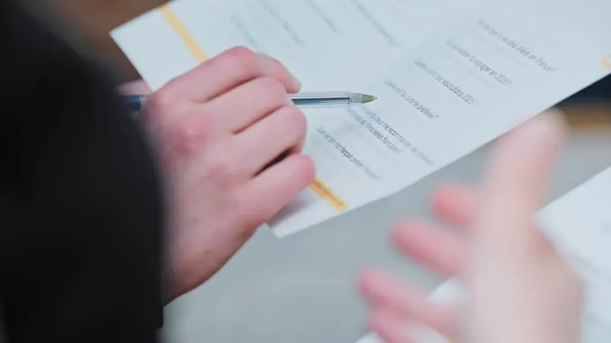 Close-up of a hand holding a pen over a printed sheet of French conversation questions during a Learn French in Vancouver activity